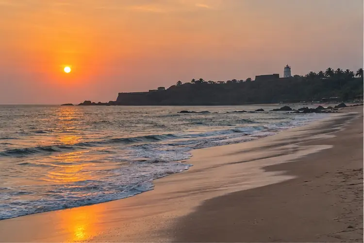 Candolim beach in Goa at sunset, Fort Aguada and its lighthouse on the headland